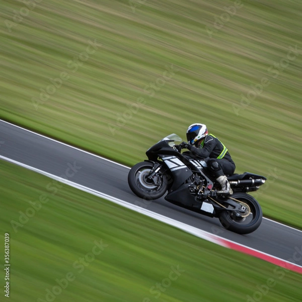 Fototapeta A panning shot of a black racing bike cornering on a track