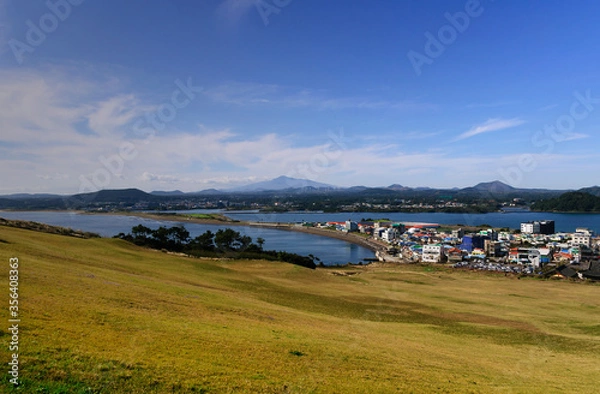 Fototapeta awesome view of seaside small city within seongsun ilchubong jeju island south korea with yellowish grass foreground and slightly cloudy blue sky and ocean. Visible at far is mountain area