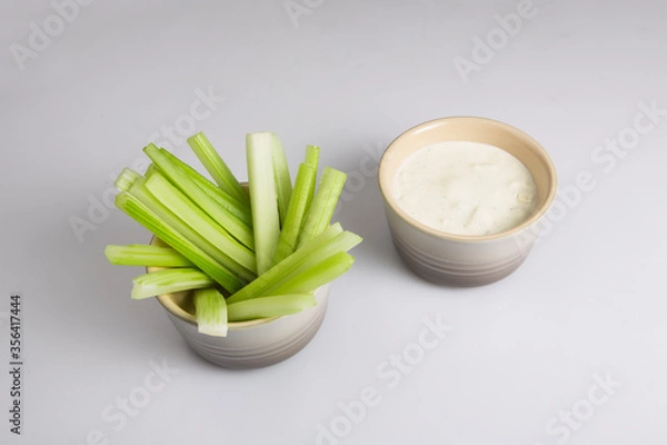 Fototapeta close up isolated top corner view shot of a bowl of crunchy juicy green celery sticks next to a white cup of blue cheese dipping sauce on a white background