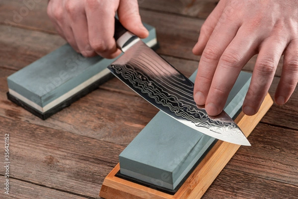 Obraz Man sharpens a Gyuto knife using a whetstone