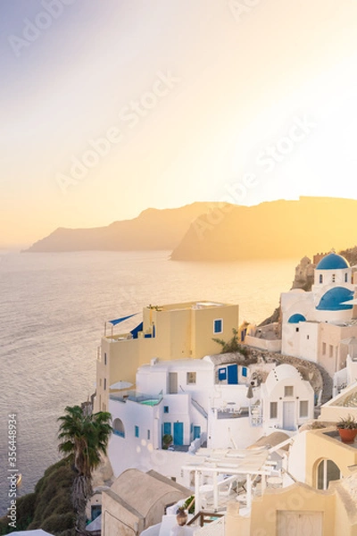 Fototapeta Sunset view of Oia with blue domes ( Saint Nikolaos Peramataris )and bell tower, Thirasia in the back, Santorini island, Cyclades, Greece
