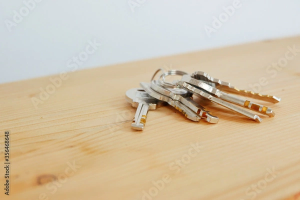 Fototapeta Bunch of keys on a shaped keychain at wooden table background. Concept for real estate or renting home with copy space,Close up.
