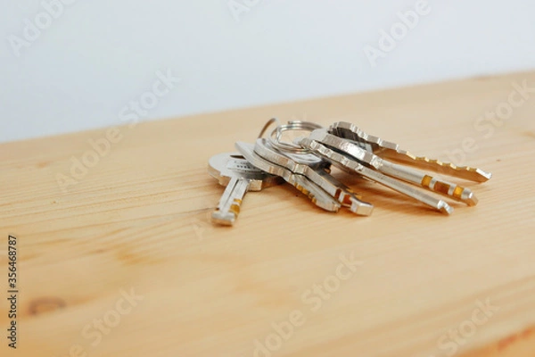 Fototapeta Bunch of keys on a shaped keychain at wooden table background. Concept for real estate or renting home with copy space,Close up.
