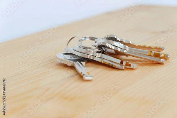 Fototapeta Bunch of keys on a shaped keychain at wooden table background. Concept for real estate or renting home with copy space,Close up.
