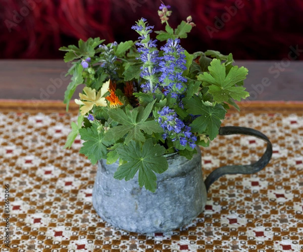 Fototapeta Colorful wild flowers arranged in a copper vessel on a patterned tablecloth in a country house.