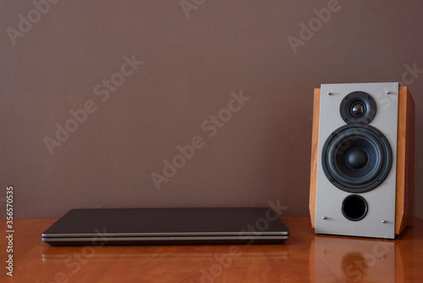 Obraz Work place - laptop and music speaker. Wooden table. Background brown wall with copy space.