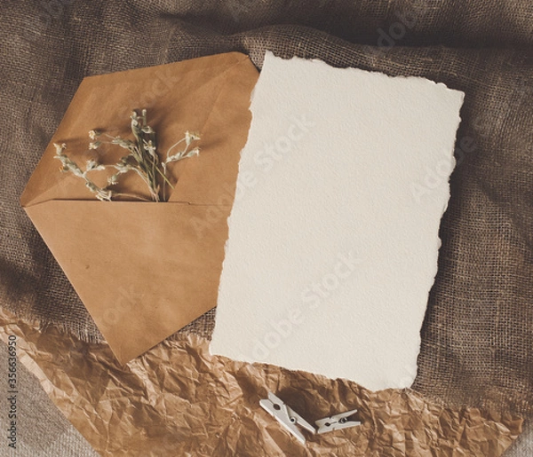 Fototapeta Cerastium dry flower, white empty paper sheet, envelope on natural brown craft sackcloth fabric and crumpled paper flat layout flat-lay top view. Design template for card, invitation, wedding decor