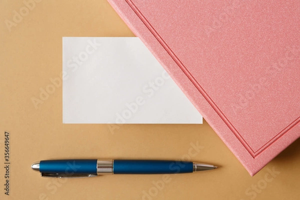 Obraz blank white business card, pink diary and metallic blue pen on a brown background flat lay