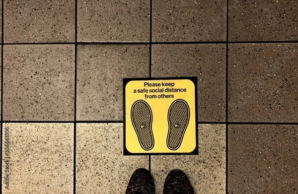 Fototapeta Newyork , usa - 8 June ,2020 : Closeup of feet standing onthe floor with yellow social distance sign - image  