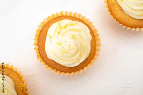 Fototapeta Three frosted cupcakes arranged on diagonal line through centre of the image.  Plain background with copy text space and shot in flat lay top down view.