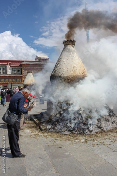 Fototapeta Smoking sangkang incense burner on Barkhor square with a man pilgrim wearing shaggy cloak in a bow with hat off