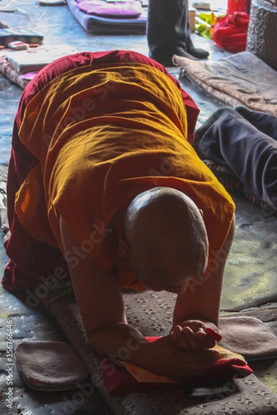 Fototapeta An old bold monk wearing traditional red and yellow cloathes praying in prostration in front of Jokhang temple in Lhasa on Barkhor square, Tibet