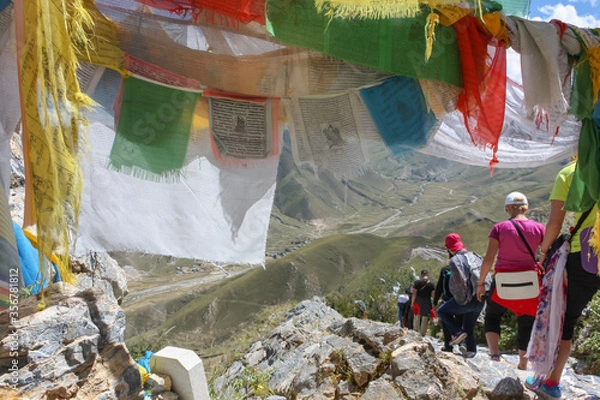 Fototapeta Group of tourists taking a hike around Drepung monastery near Lhasa, Tibet, walking underneath prayer flags