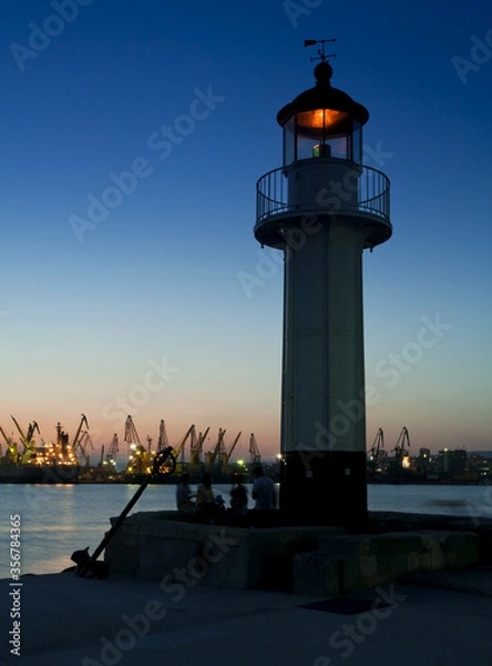 Fototapeta Sea lighthouse and passing boat at sunset over the port of Varna, Bulgaria.