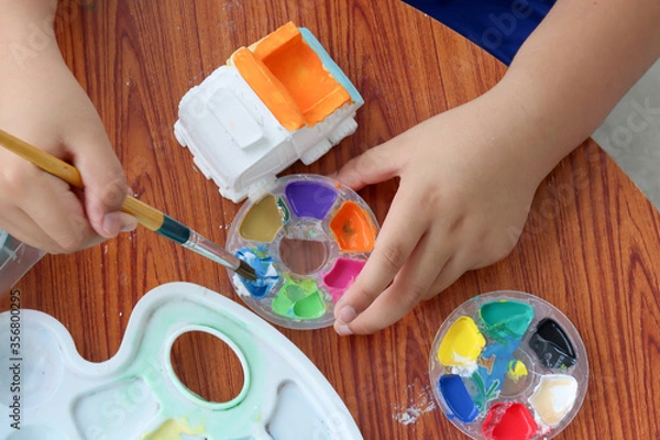 Obraz Cute little boy hands painting Plaster doll at the table with art supplies, top view.