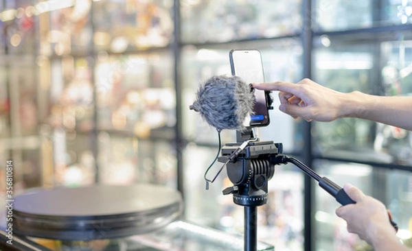 Fototapeta Male hand is shooting a video using gimbal and smart phone on tripod for live about the product for sell ans show the details of products