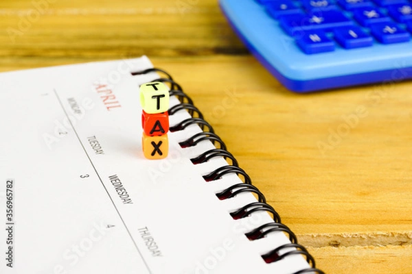Fototapeta Conceptual image of tax return to tax authority in April. Stacked alphabet beads TAX on calendar on April month of calendar. Selective focus on beads. Wooden background. Calculator visible.