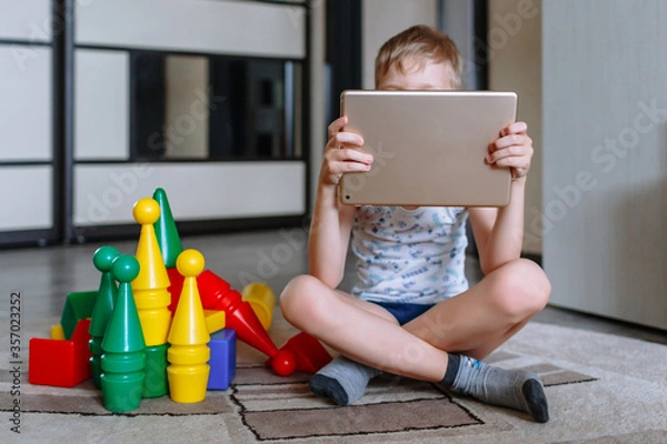 Obraz The boy is in the game room, next to toys, but does not play, but looks at the tablet