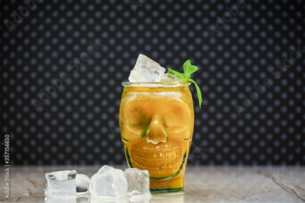 Obraz Peach juice in a skull-shaped glass at a marble board with pieces of ice. Fresh peach juice, ice and an unusual mug in shape of a head. Halloween zombie cocktail in a glass skull-shaped.