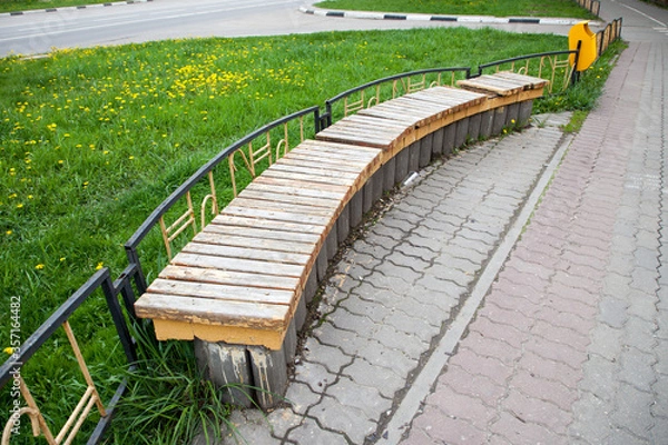 Fototapeta Wooden bench near a metal fence on a footpath