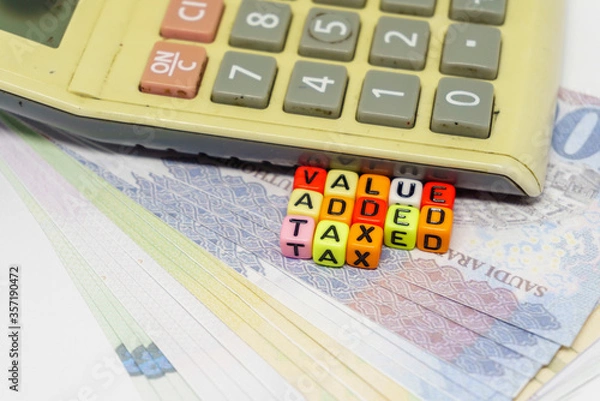 Fototapeta Conceptual value-added tax rollout in Saudi Arabia. Value added tax texts on colorful alphabet beads and calculator over riyals notes. Focus on beads; others in gradient blur.