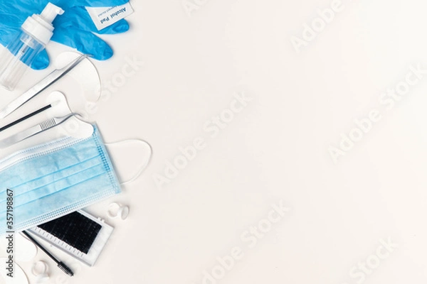 Fototapeta Beauty flat lay with treatment products and personal protective equipment (PPE) needed by beauty salons due to corona virus.  Plain light background with items on left side of frame and copy space