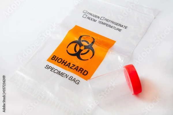 Obraz Biohazard bag with plastic bottle for sputum specimen collection on white background. Concept of lab test for diagnosis of coronavirus infection. Selective focus