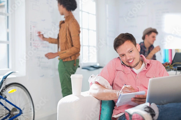 Fototapeta Businessman taking notes on phone in office