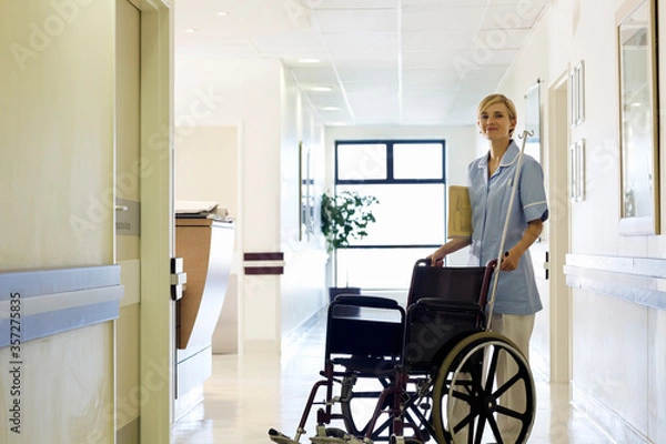 Fototapeta Nurse pushing wheelchair in hospital hallway