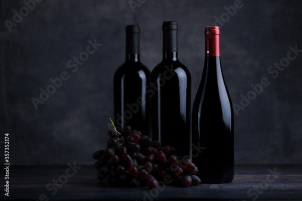 Fototapeta The red wine in the glass, along with a bottle of wine made from red grapes, is laid on a wooden floor and a beautiful backdrop. Ready for partying