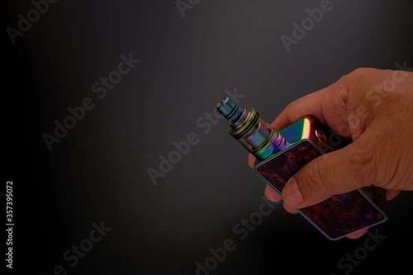 Fototapeta Conceptual of recent uncertainty of health safety of e-cigarette. Isolated close-up hand holding vaping kit.
