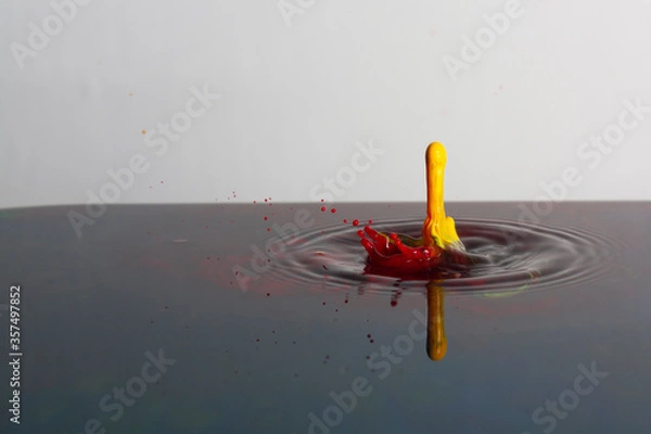 Fototapeta Splash of bright paint in still water. Drop of toxic yellow and red paint falling on calm surface of clean water and causing ripples