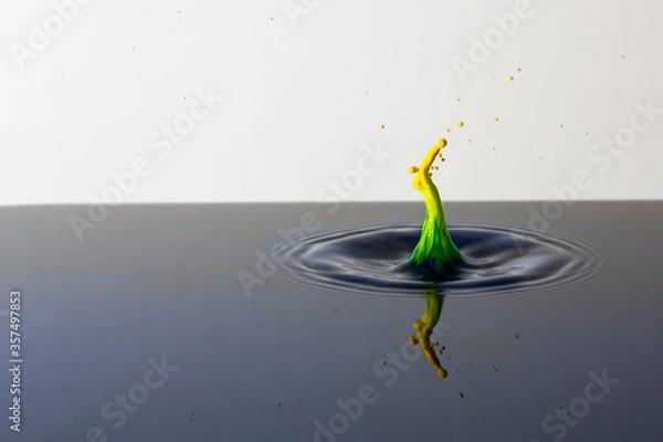 Fototapeta Splash of bright paint in still water. Drop of toxic yellow and green paint falling on calm surface of clean water and causing ripples