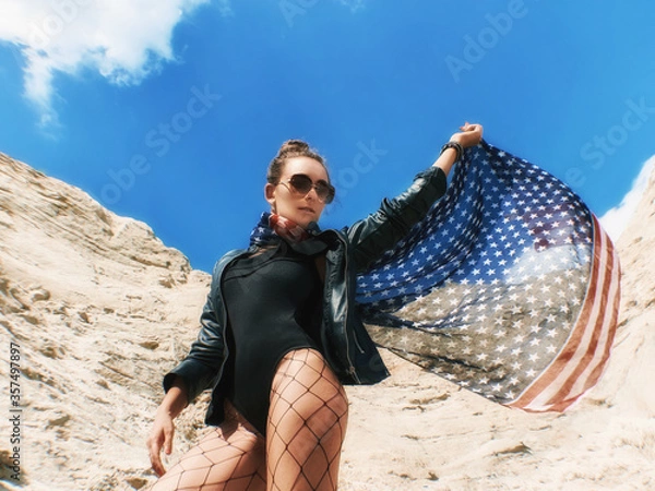 Obraz Model Girl holding the american flag and looking ahead in desert. The american flag keeping in the wind. Copy space