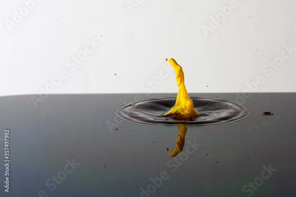 Fototapeta Splash of bright paint in still water. Drop of toxic yellow paint falling on calm surface of clean water and causing ripples