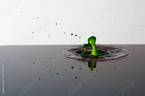 Fototapeta Splash of bright paint in still water. Drop of toxic green and yellow paint falling on calm surface of clean water and causing ripples
