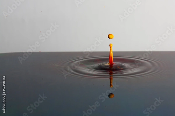 Fototapeta Splash of bright paint in still water. Drop of toxic yellow and red paint falling on calm surface of clean water and causing ripples