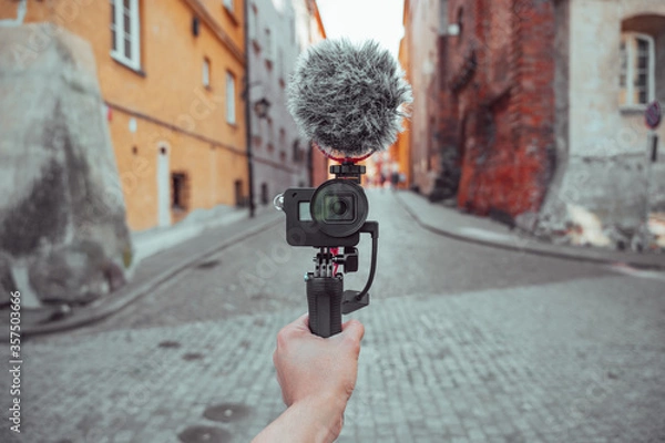 Obraz Hand holding a camera with microphone, vlogger with camera recording a video blog, content creation tools