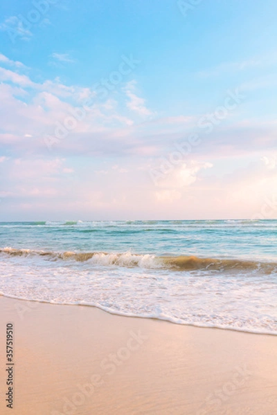 Fototapeta Sandy beach pastel background. Blue cloudy sky and soft ocean wave in warm sunset light