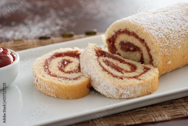 Fototapeta delicious roll cake with guava cream jelly and sugar sliced on white platter and blurred background