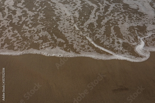 Fototapeta White foam on waves coming to shore on summer beach