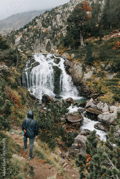 Fototapeta Lonely man watching a waterfall in nature of Benasque Valley, surrounded by the highest peaks in that range, located in the heart of the Pyrenees, Aragón, Spain
