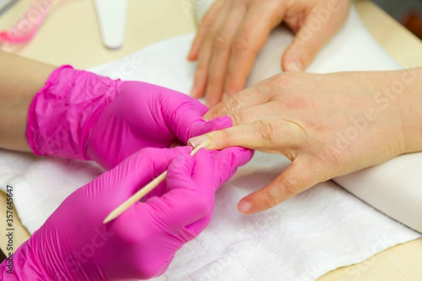 Fototapeta Nail care. Closeup of beautiful woman hands getting manicure in spa salon. Female manicurist cleaning cuticle with professional manicure pusher tool. Cosmetic procedure..