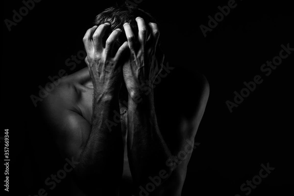 Obraz Man covers his face with his hands. Regret or fear. On a dark background. Black and white photography.