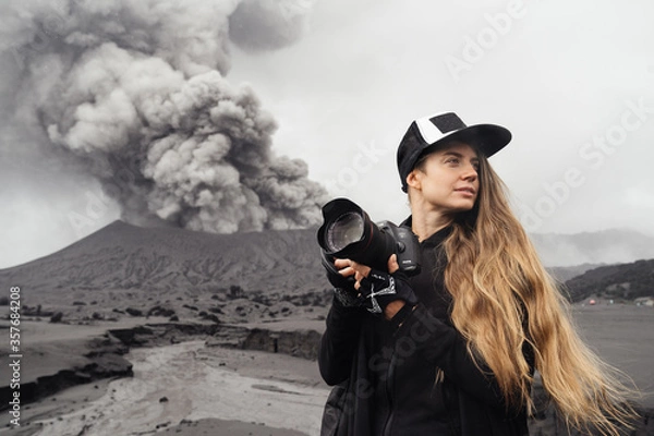 Obraz girl travel photographer stands with camera against the backdrop of an erupting volcano