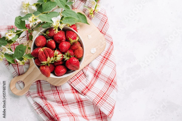Fototapeta Fresh garden strawberry in a plate on a wooden board with a beautiful napkin and a serving and a sprig of jasmine inflorescences, wholesome food and vitamins. Top view layout with place for text.
