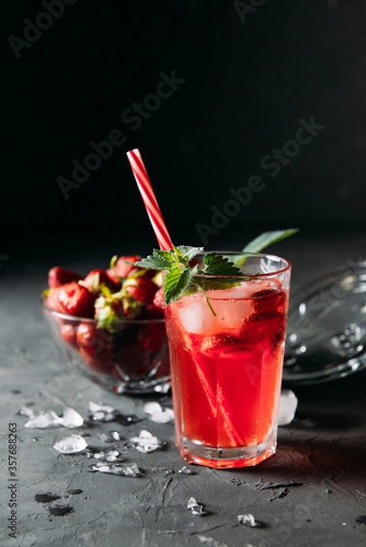 Fototapeta A refreshing summer drink made from strawberries and mint, juice, soda with ice cubes and slices of berries, in a beautiful glass with water droplets on a wooden board, dark background, vertical photo