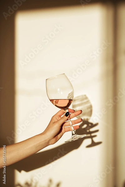 Fototapeta Glass of pink wine in hand with shadow on the wall