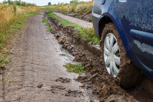 Fototapeta A muddy unpaved rural road and a car wheel in the mud