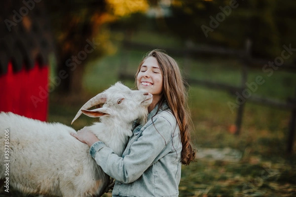 Obraz Portrait of teen girl hugging with a white goat in a farm. Copy space.